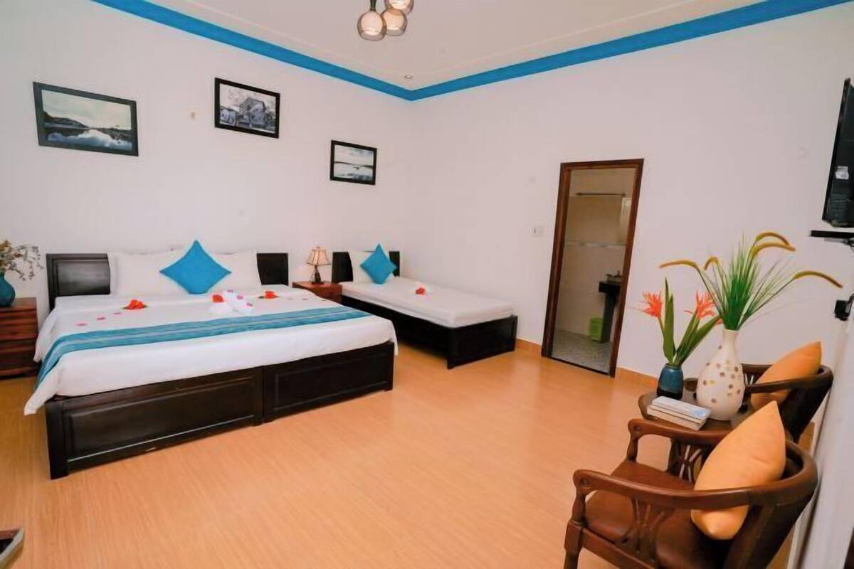 A hotel room with a large bed, two smaller beds, a wooden chair, and a TV.