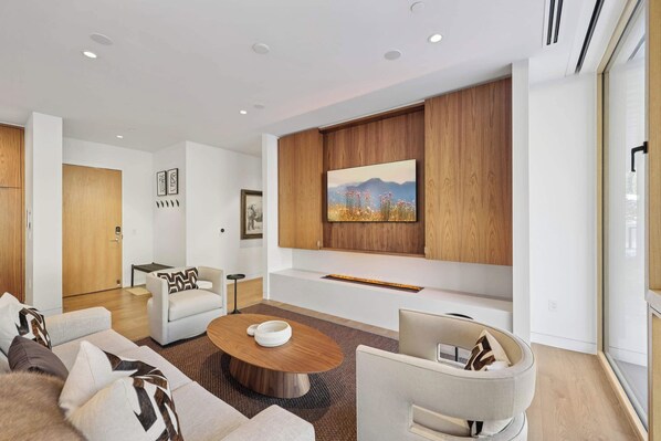 A modern living room with a sofa, armchairs, a coffee table, and a large wall-mounted TV.