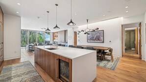 A modern kitchen with a central island, pendant lighting, and a dining area with a wooden table and chairs.