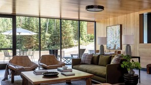 A modern living room with large windows, leather chairs, a wooden coffee table, and a sofa.