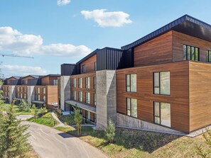 Un immeuble résidentiel moderne comprenant plusieurs logements, de grandes fenêtres et un toit en pente.