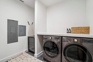 Une buanderie équipée de deux machines à laver, d’un sèche-linge et d’une petite étagère où sont rangés les produits de toilette.