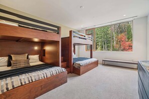 Une chambre avec deux lits superposés, une grande fenêtre donnant sur la forêt et un banc intégré.