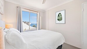 A hotel room with a bed, a window with curtains, a framed plant, and a lamp. - Bella Vista 19 Waterfront views (Shoal Bay)