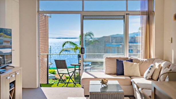 A modern living room with a balcony overlooking a beach. - Bella Vista 19 Waterfront views (Shoal Bay)