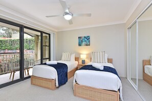Ein Hotelzimmer mit zwei Betten, einem Deckenventilator, einem Gemälde, einem Nachttisch mit Lampe und Blick ins Freie.