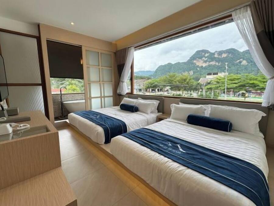 A hotel room with two beds, a bathroom, and a large window offering a mountain view.