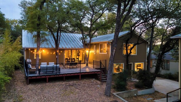 Une maison à deux étages avec une terrasse, entourée d’arbres.