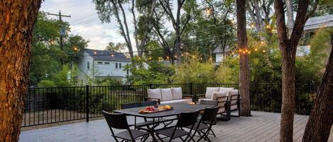 An outdoor deck with a dining table and chairs, surrounded by trees and string lights.