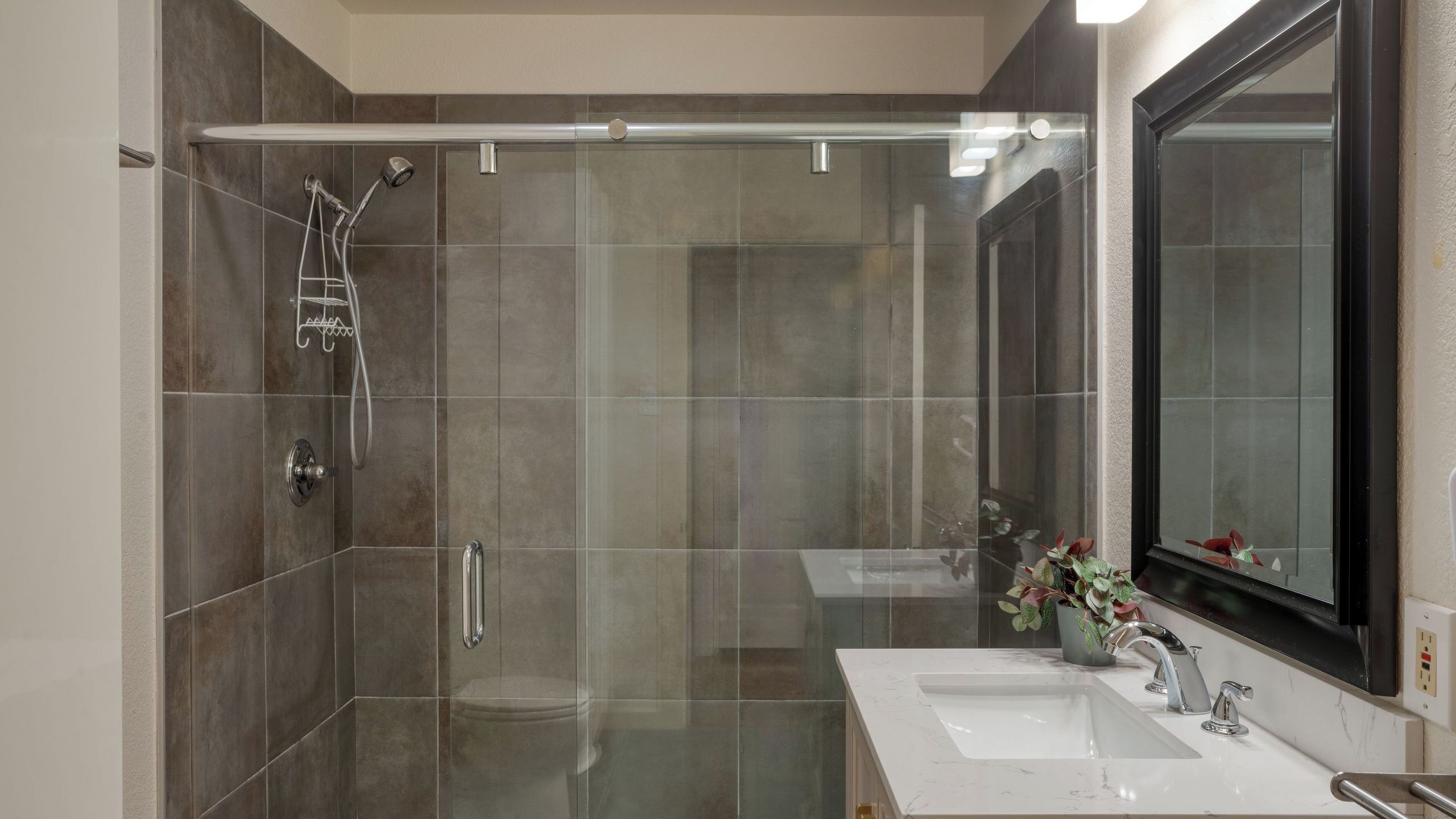 Un baño moderno con ducha de vidrio, lavamanos blanco y un espejo grande.
