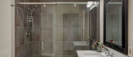 Un baño moderno con ducha de vidrio, lavamanos blanco y un espejo grande.