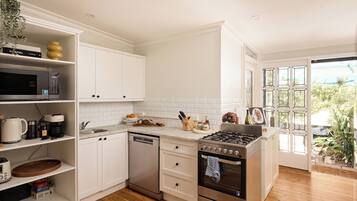 A modern kitchen with white cabinets, a dishwasher, a stove, and a sink. There is a window with a view of greenery outside.