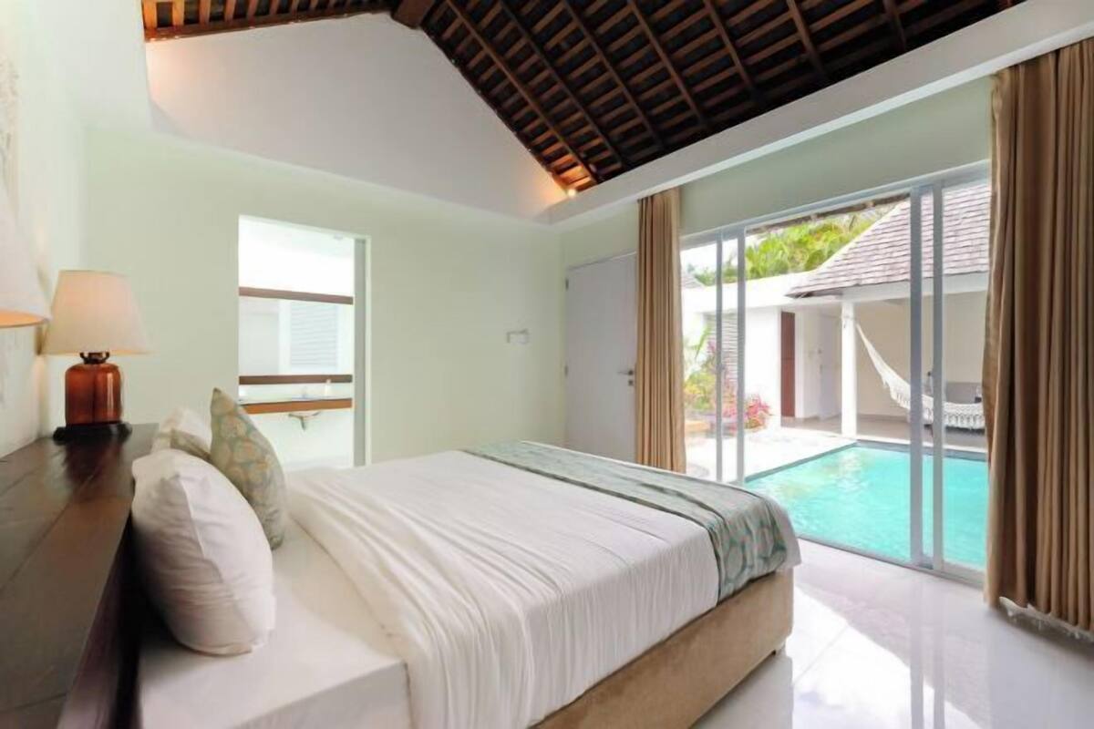 Un dormitorio con cama, mesita de noche, lámpara y vista a una piscina.