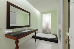 Un baño con tocador de madera, un espejo grande, un lavamanos blanco, una bañera y una puerta de ducha de vidrio esmerilado.