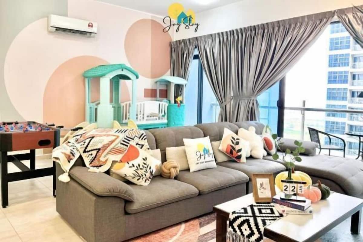 A living room with a sofa, a coffee table, a foosball table, and a window with curtains.