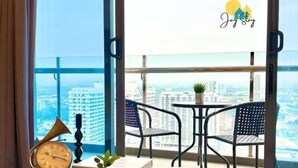 Een balkon met uitzicht op een stadsgezicht, een tafeltje met stoelen, een klok en een bloempot.
