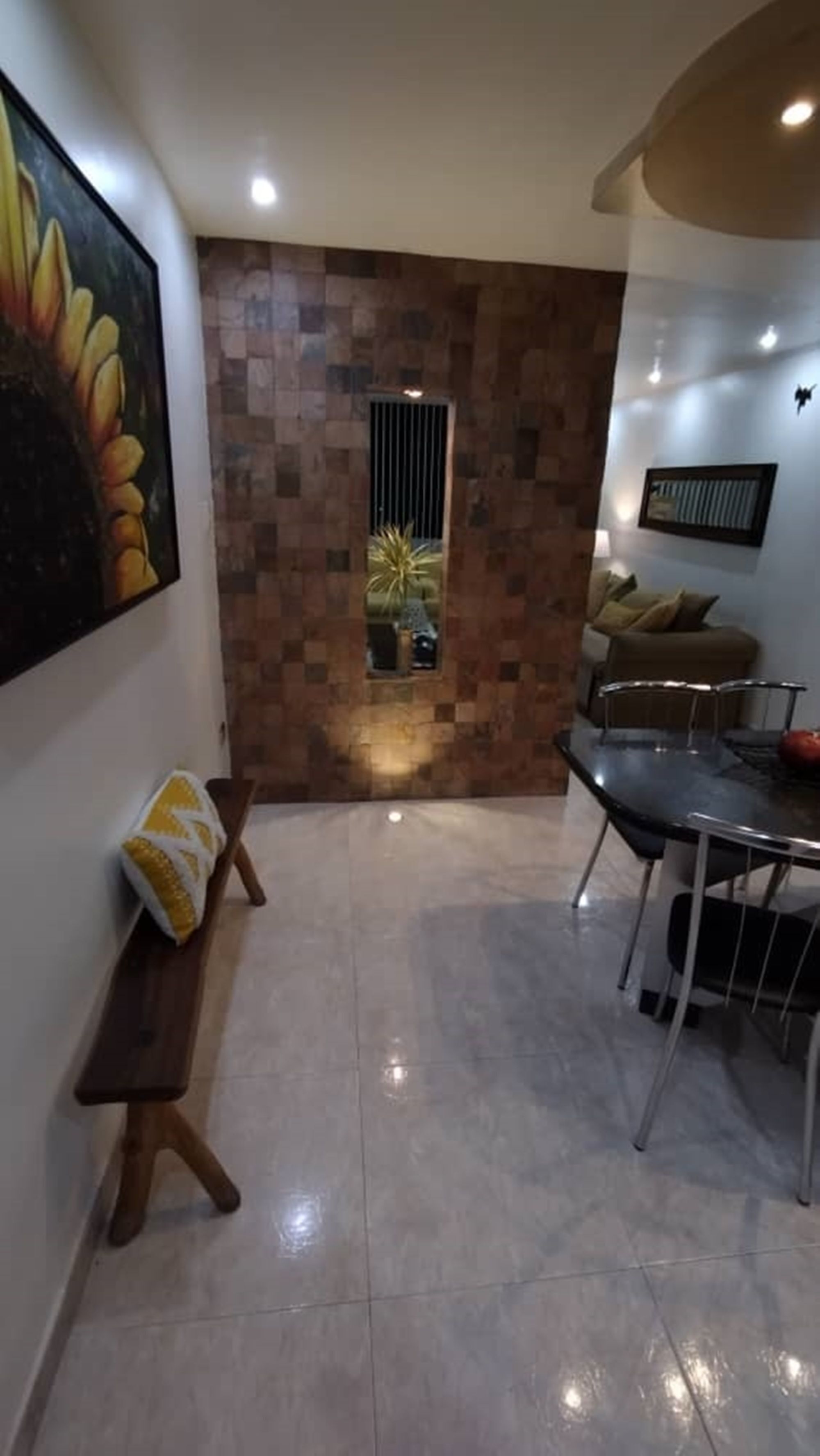 Uma sala de estar moderna com piso de azulejos, um espaço de refeições com mesa e cadeiras, um sofá e um quadro de girassóis na parede.