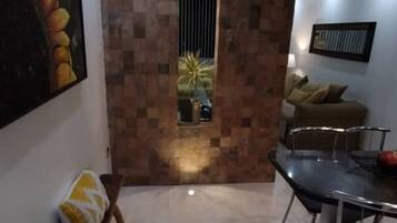 Uma sala de estar moderna com piso de azulejos, um espaço de refeições com mesa e cadeiras, um sofá e um quadro de girassóis na parede.
