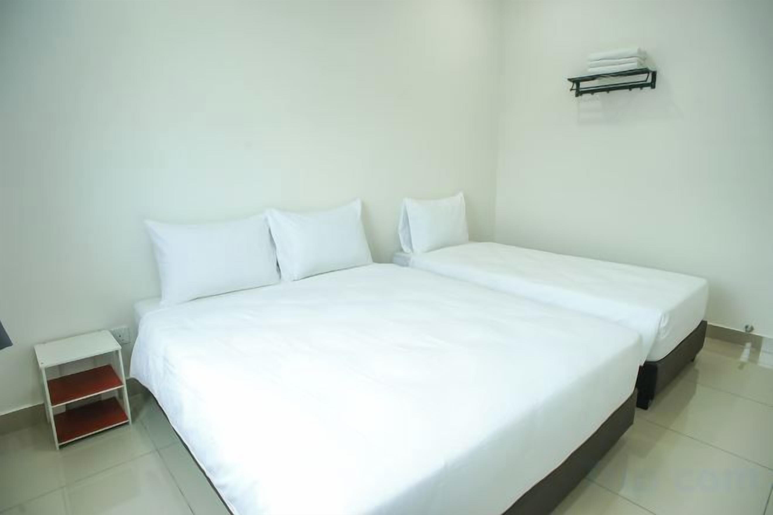 Una habitación de hotel limpia y blanca con una cama individual, una mesita de noche pequeña y un equipo de aire acondicionado instalado en la pared.