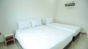 Una habitación de hotel limpia y blanca con una cama individual, una mesita de noche pequeña y un equipo de aire acondicionado instalado en la pared.