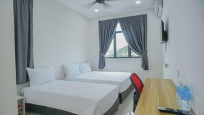 Ein Hotelzimmer mit zwei Betten, einem Schreibtisch, einem Stuhl, einem Deckenventilator und einem fensterbelaubten Fenster.