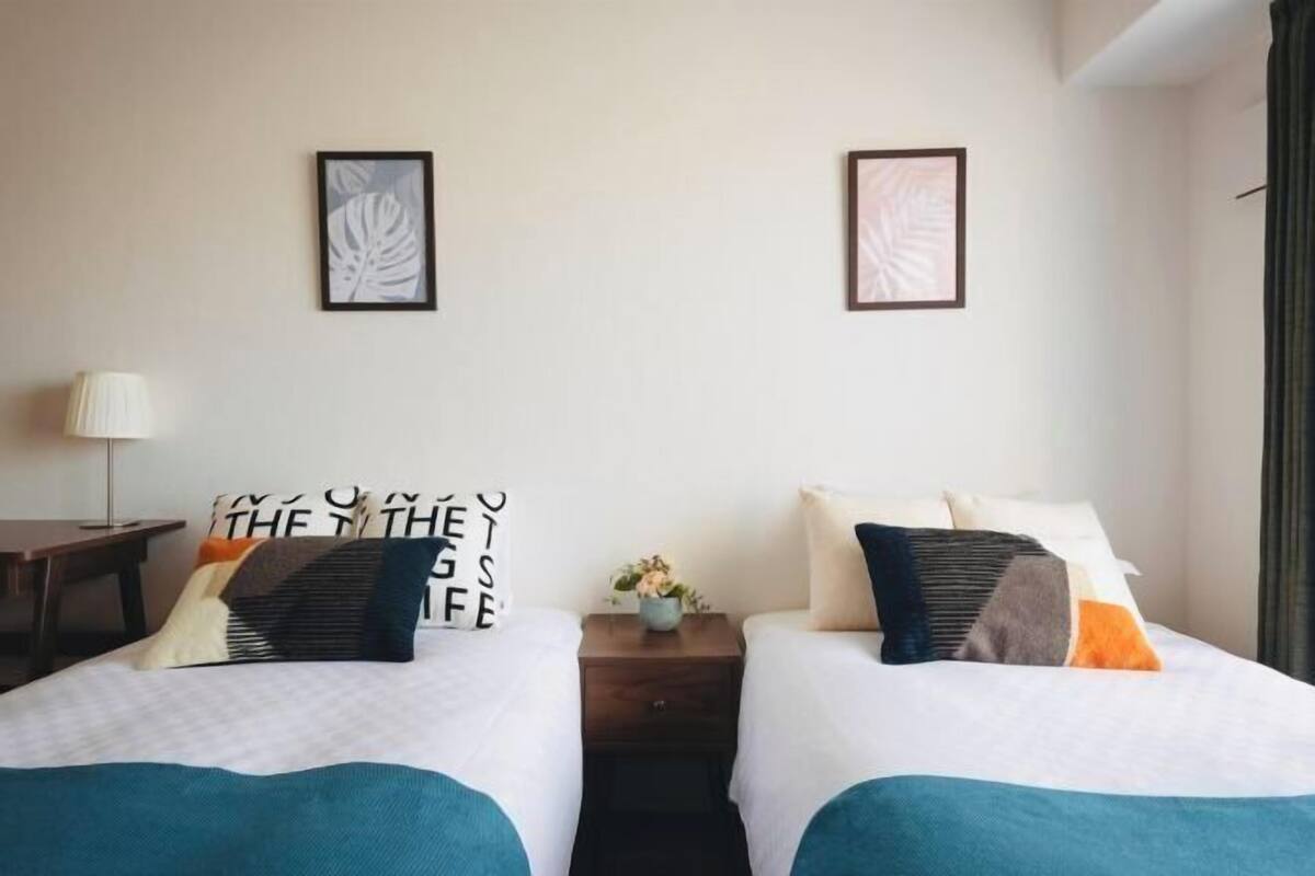 A hotel room with two beds, a nightstand, a lamp, and framed artwork on the walls.