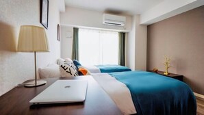 Una habitación de hotel con una cama, un escritorio con una computadora portátil, una lámpara y aire acondicionado.