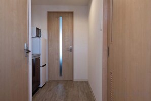 Un pasillo estrecho con una puerta de madera al final, un refrigerador blanco y un microondas en un estante.