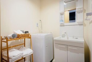 A bathroom with a white sink, mirror, and a drying rack with towels. - Tanimachikun Star Hotel Kujo 27 (Osaka)