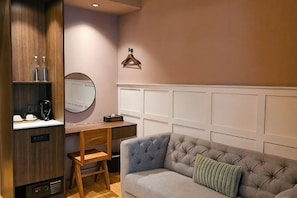 A room with a grey sofa, a wooden desk with a mirror, and a white panelled wall. - The Palm Suite at Lava Mansion (George Town)