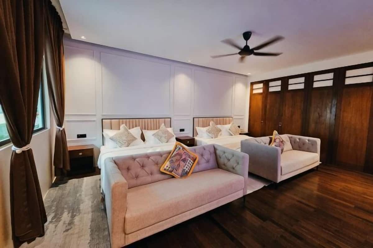 A bedroom with a bed, two sofas, a ceiling fan, and wooden paneling.