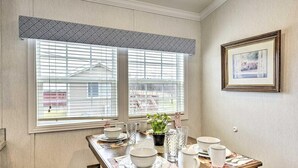 A dining area with a table set for four, two windows with blinds, a framed picture on the wall, and a potted plant on the windowsill. - Twin Cottage Retreat · Poconos Luxury Stay (Pleasant Mount)