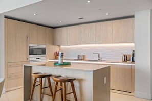 Eine moderne Küche mit Holzschränken, einer zentralen Kochinsel mit Hockern, einem eingebauten Backofen und einer eleganten Spritzschutzwand.