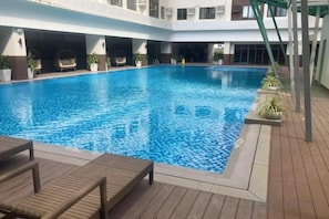 An indoor swimming pool with lounge chairs and potted plants. - By Trixia BE Apartments, Luxury Studio Apartments near IT Park (Cebu City)