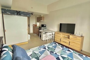 Una camera da letto moderna con un letto, una TV, un comò in legno e una piccola cucina sullo sfondo.