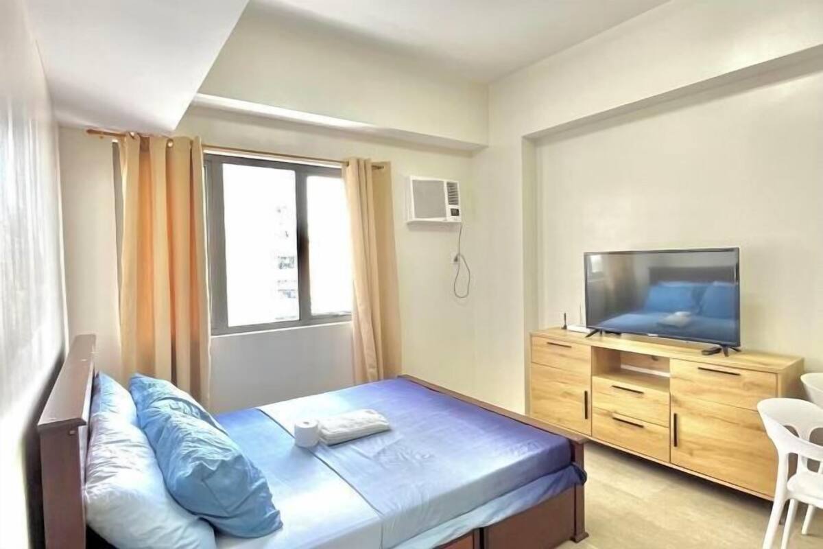 Ein Hotelzimmer mit Bett, Fernseher, Holzschrank und Fenster mit Vorhängen.