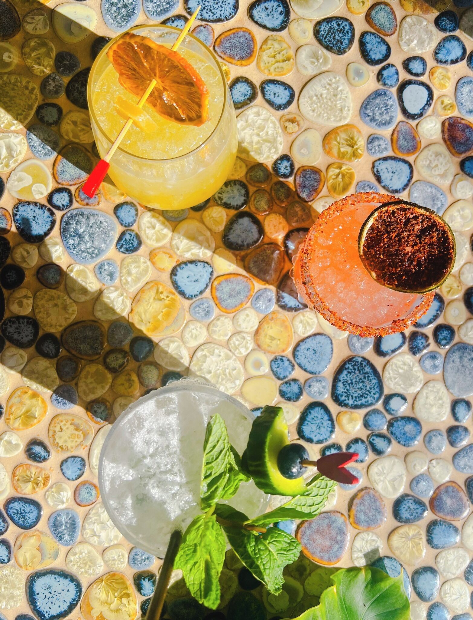 A table with three drinks, a mint garnish, and a decorative tile pattern.