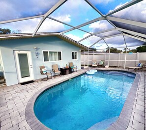 A swimming pool with a covered patio area, chairs, and a door.