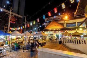 A bustling street market at night with food stalls and a prominent building with a sign. - Hometel Night Bazaar Chiangmai (Chiang Mai)