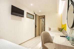 Habitación de hotel con cama, escritorio, silla, televisión, espejo y puerta al baño.