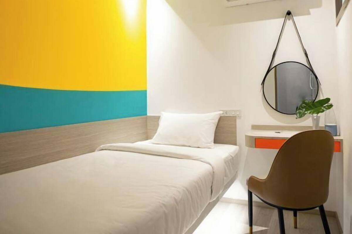 A hotel room with a bed, a chair, a round mirror, and a plant.