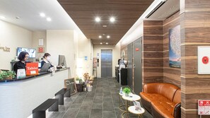 A hotel reception area with a reception desk, two staff members, a vending machine, a sofa, and a fire extinguisher. - Dream Inn Hakata (Fukuoka)