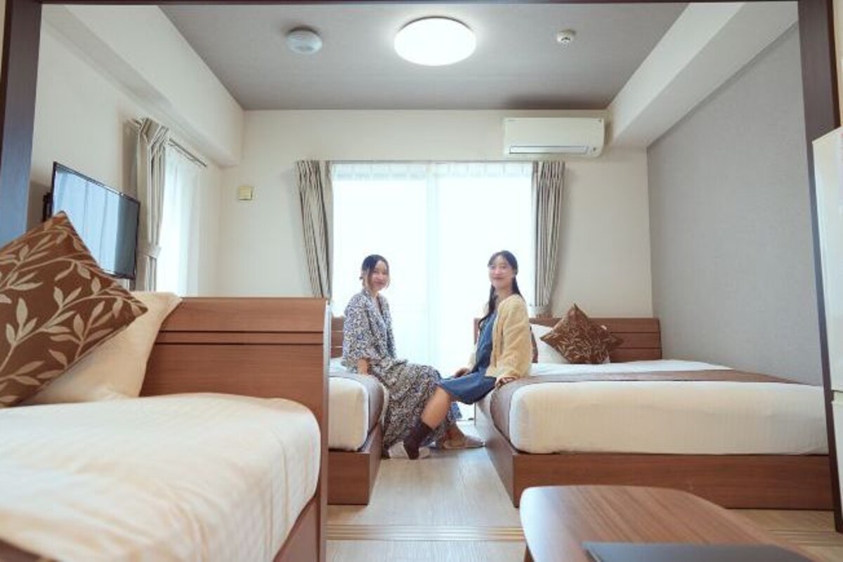A hotel room with two single beds, a TV, and an air conditioning unit.