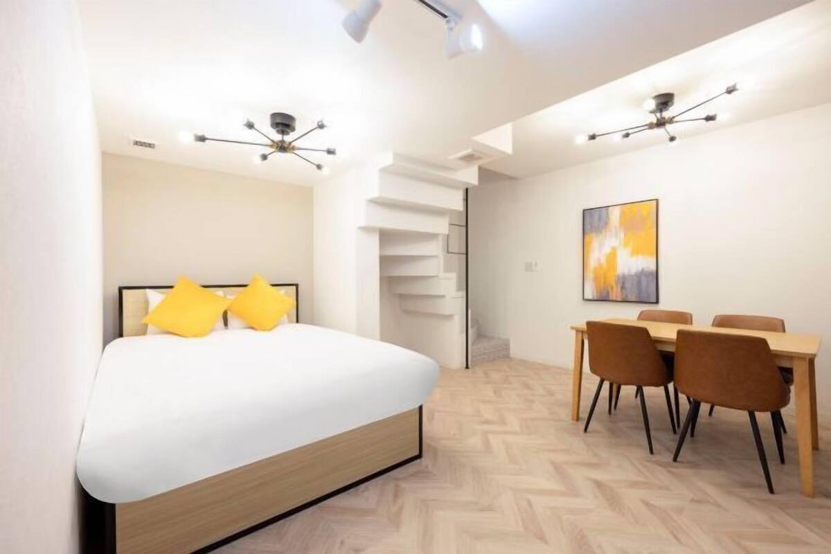 A modern bedroom with a bed, a dining area with chairs, and a staircase.