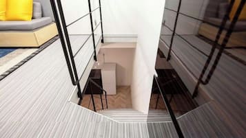 A modern interior with a staircase leading to a lower level, a sofa with a yellow cushion, and a patterned floor.
