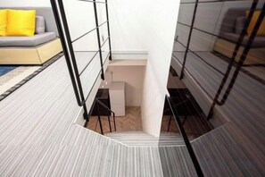 A modern interior with a staircase leading to a lower level, a sofa with a yellow cushion, and a patterned floor. - HJ Place Shibuya (Tokyo)