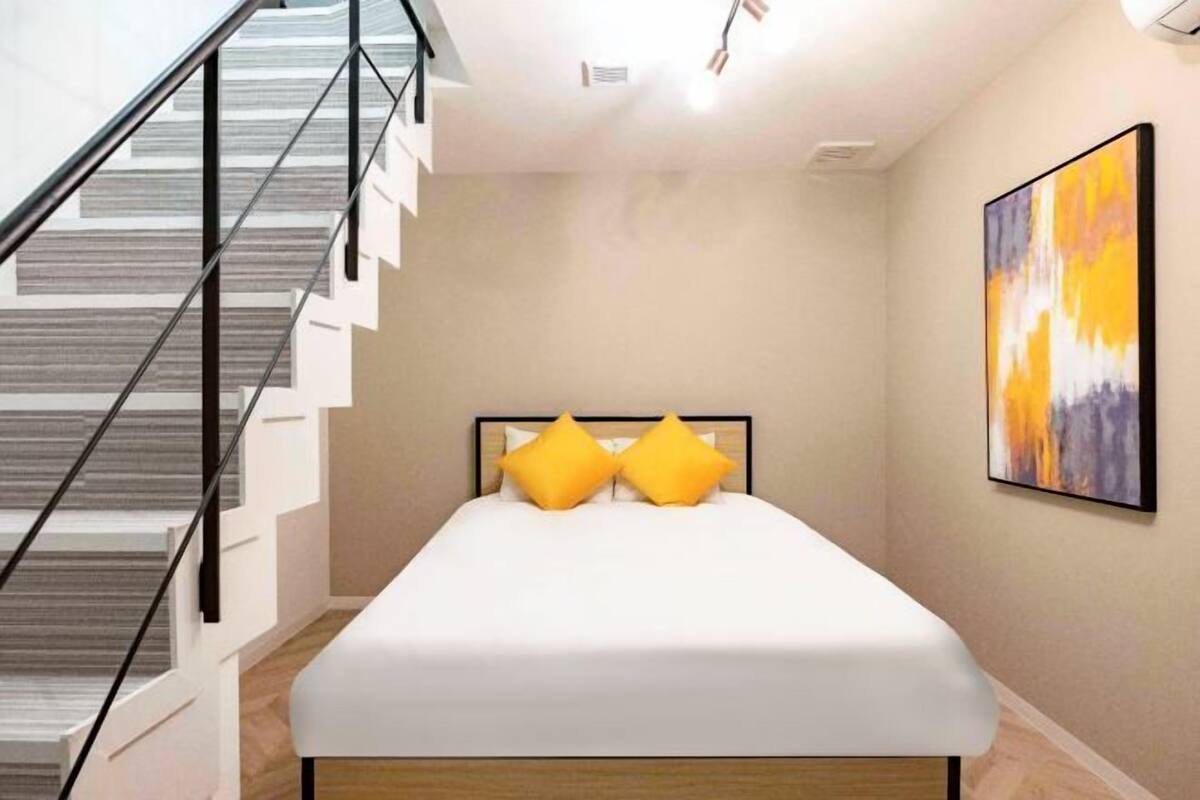 A bedroom with a bed, a staircase, and a painting on the wall.