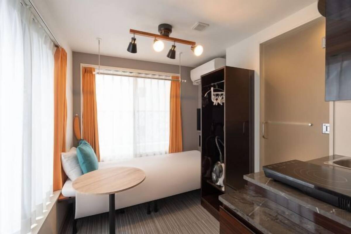 A modern hotel room with a sofa, a small round table, a built-in wardrobe, and a shower area.