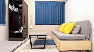 A compact living space with a grey sofa, a small table, a wardrobe, and a window with blue curtains.