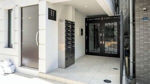 A building entrance with a metal gate, a set of lockers, and a sign above the door. - HJ Place Shibuya (Tokyo)